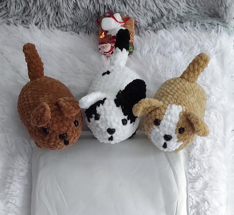 May include: Three crocheted stuffed dog toys. One is brown, one is white with black spots, and one is tan with white spots.