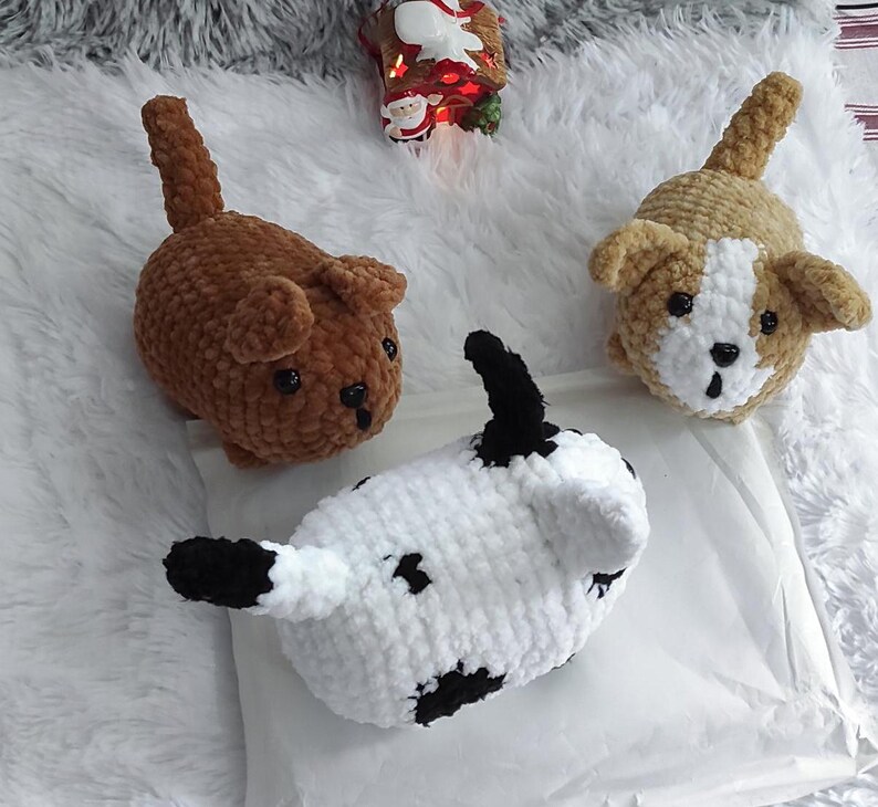 May include: Three crocheted stuffed animals shaped like dogs. One is brown, one is white with black spots, and one is tan with white accents.