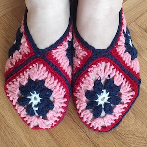 Peut inclure: Une paire de pantoufles crochetées avec un motif rose, rouge et bleu marine. Les pantoufles ont un motif de fleur au centre.