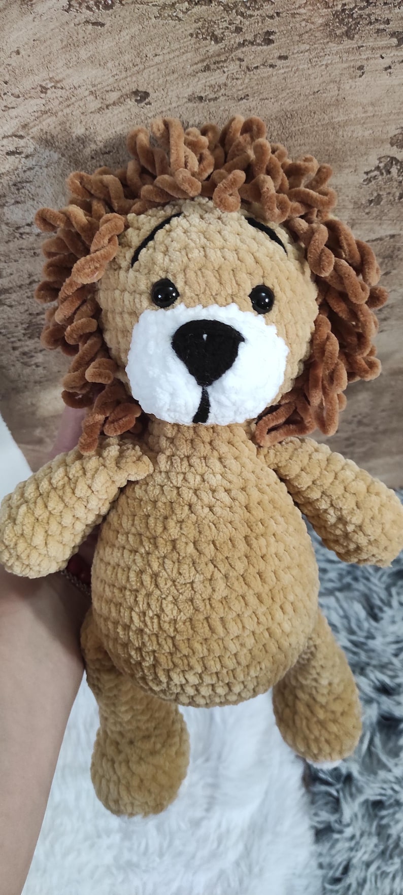 May include: A handmade plush lion toy with a tan body, brown mane, and a white muzzle. The lion has black eyes and is made of soft, textured yarn. A cuddly stuffed animal.