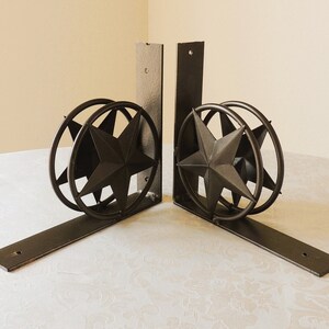May include: Two black metal shelf brackets with a star design. The brackets are angled and have a decorative star in the center of each.