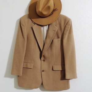 May include: A tan blazer with a brown fedora hat on top. The blazer has a two-button closure and two pockets.