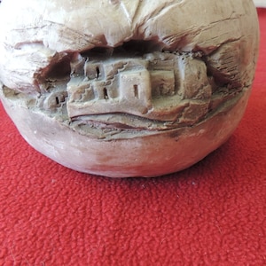 May include: A white ceramic sphere with a carved depiction of a small village nestled in a mountainside.