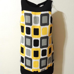 May include: Sleeveless dress with a black neckline and hem. The body of the dress features a repeating pattern of yellow, gray, and black squares on a white background. The dress is displayed on a black hanger.
