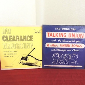 May include: Two square vinyl record covers side by side. The left cover is yellow with black text reading IFR CLEARANCE RECORDING FOR MAINTAINING IFR SHORTHAND PROFICIENCY and a drawing of a hand writing. The right cover is blue with white and red text.