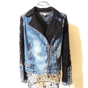 May include: A blue denim jacket with black lace sleeves and collar. The jacket has a zipper closure and multiple pockets. The sleeves are long and made of a delicate black lace material.