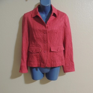 May include: A pink blazer with a textured fabric and four buttons. The blazer has two pockets on the front.