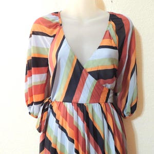 May include: A colorful wrap dress with a V-neckline and long sleeves. The dress features vertical stripes in shades of orange, red, black, white, and blue. The dress is tied at the waist with a matching fabric belt.