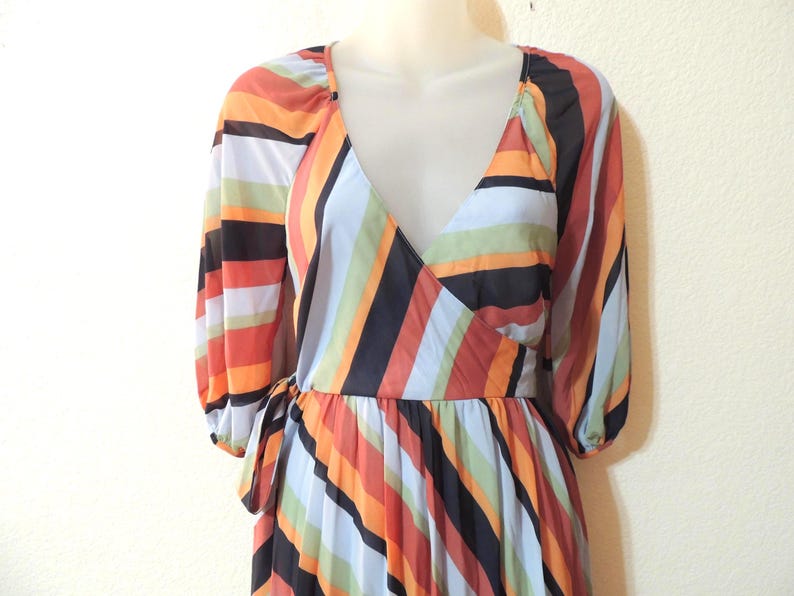 May include: A colorful wrap dress with a V-neckline and long sleeves. The dress features vertical stripes in shades of orange, red, black, white, and blue. The dress is tied at the waist with a matching fabric belt.