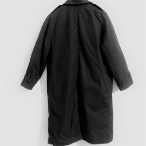 May include: A black long-sleeved trench coat hanging on a hanger. The coat has a collar and a single row of buttons down the front.