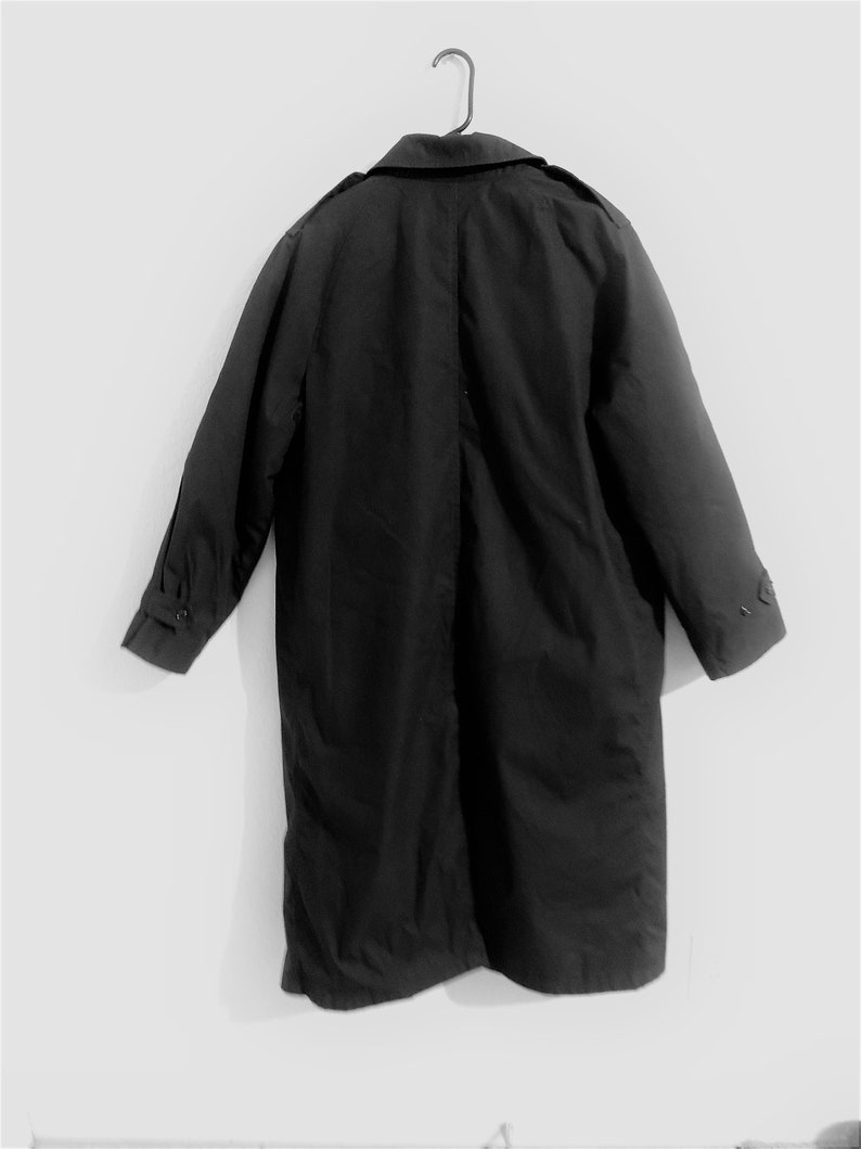May include: A black long-sleeved trench coat hanging on a hanger. The coat has a collar and a single row of buttons down the front.