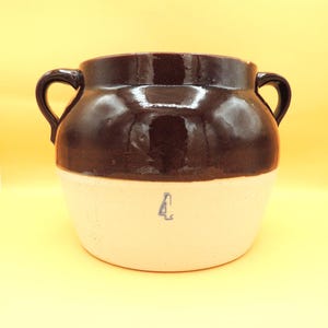 May include: A two-toned stoneware crock with a dark brown glazed top and handles, and a cream-colored base. The number "4" is stenciled in blue on the base. This vintage kitchenware item is ideal for rustic decor.