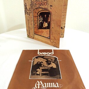 May include: A vintage Bread album cover featuring the band inside an archway, with the word "bread" at the top. The album cover is brown with a textured appearance. The album cover is open, with the record sleeve lying flat in front.