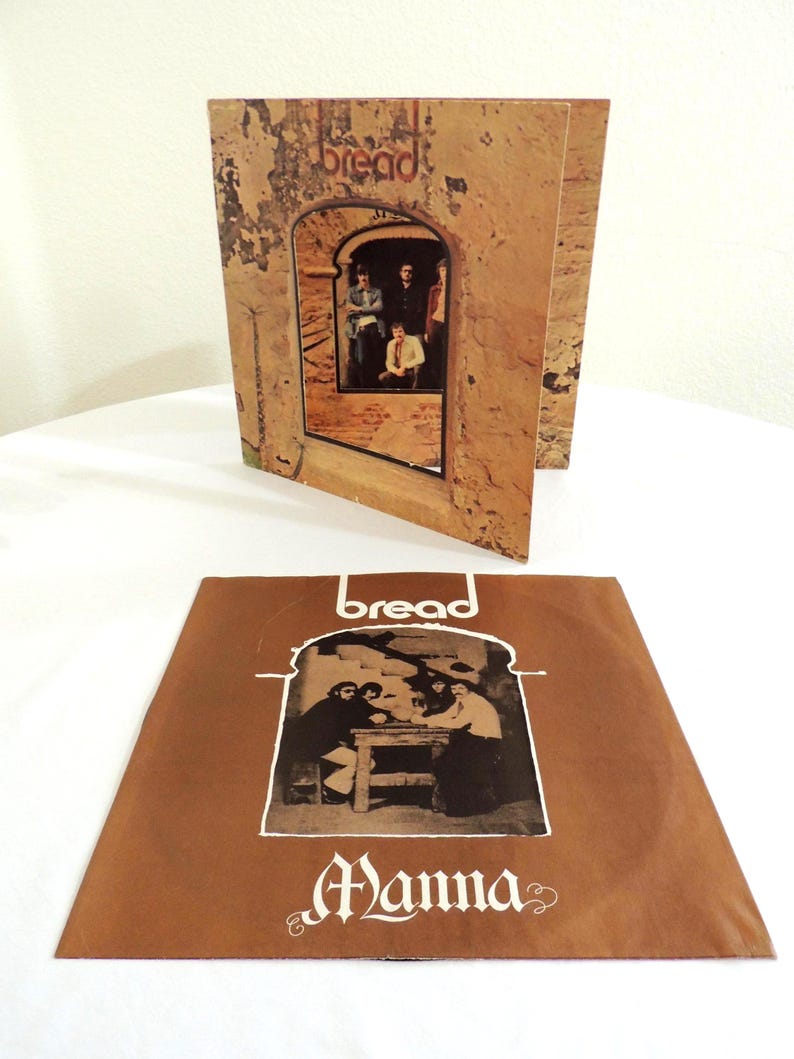 May include: A vintage Bread album cover featuring the band inside an archway, with the word "bread" at the top. The album cover is brown with a textured appearance. The album cover is open, with the record sleeve lying flat in front.