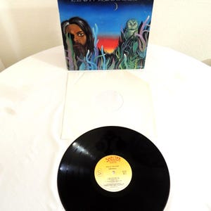 May include: A vintage vinyl record album titled "Will O' The Wisp" by Leon Russell. The album cover features a painted illustration with a portrait, an owl, and the text "Will O' The Wisp Leon Russell". The record is black with a yellow label.