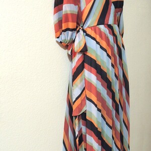 May include: A colorful, long-sleeved wrap dress with a V-neckline. The dress features vertical stripes in orange, black, red, green, and blue. The dress is tied at the waist with a matching fabric tie.