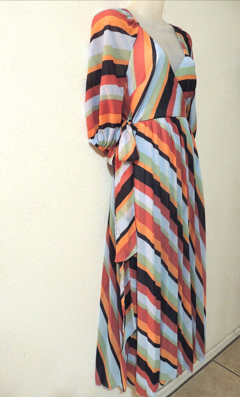 May include: A colorful, long-sleeved wrap dress with a V-neckline. The dress features vertical stripes in orange, black, red, green, and blue. The dress is tied at the waist with a matching fabric tie.