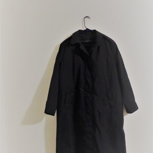 May include: A black long-sleeved coat hanging on a hanger against a white wall.