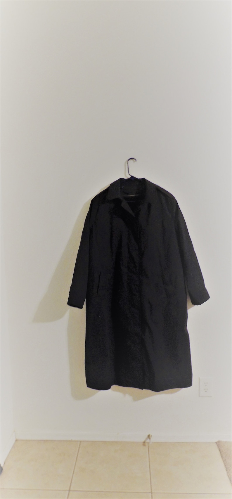 May include: A black long-sleeved coat hanging on a hanger against a white wall.