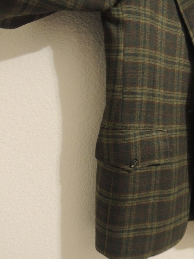 May include: A brown and green plaid blazer with a single button closure and a pocket on the left side.