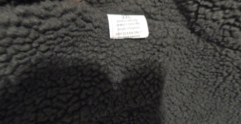 May include: A black fabric label with white text that reads "220 BAIS 01 AA SIST SPMIC 1.150 150 Acrylic DRY CLEAN ONLY DO NOT PRESS".