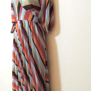 May include: A colorful, floor-length dress with a V-neck and long sleeves. The dress features vertical stripes in shades of orange, black, blue, and green. The dress is displayed on a mannequin.