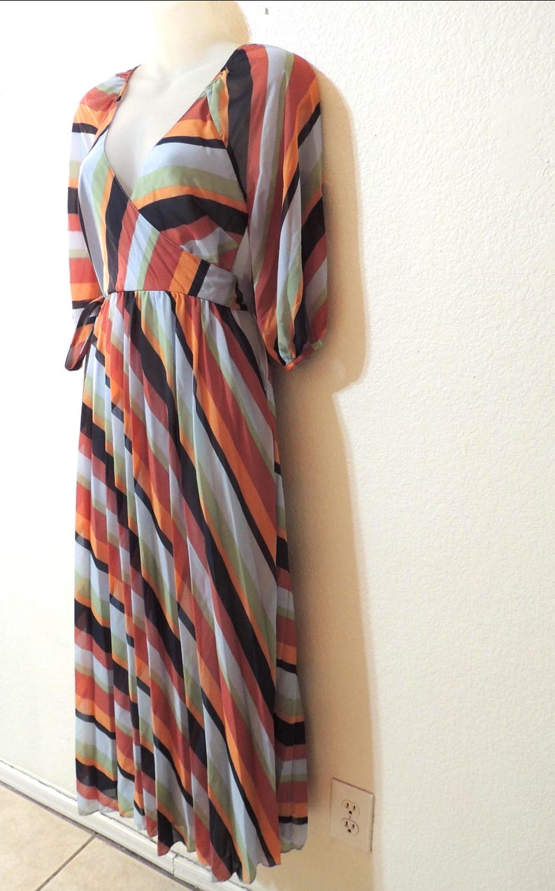 May include: A colorful, floor-length dress with a V-neck and long sleeves. The dress features vertical stripes in shades of orange, black, blue, and green. The dress is displayed on a mannequin.