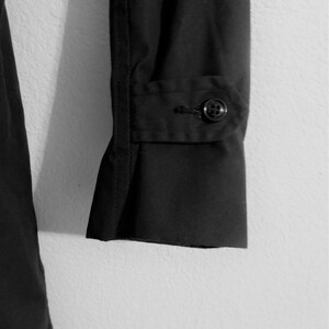 May include: Black long-sleeved shirt with a button cuff. The shirt is made of a smooth, wrinkle-resistant fabric.