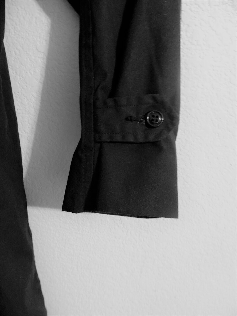 May include: Black long-sleeved shirt with a button cuff. The shirt is made of a smooth, wrinkle-resistant fabric.