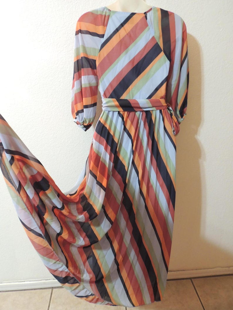 May include: A flowing, vintage maxi dress featuring a vibrant striped pattern in shades of orange, red, black, blue, and green. The dress has long sleeves, a cinched waist, and a pleated skirt, creating a flattering silhouette. The fabric appears lightweight and semi-sheer.