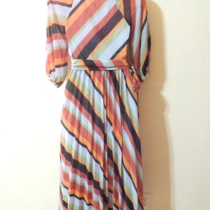 May include: A vintage, floor-length dress with a colorful striped pattern. The dress features a round neckline, long sleeves, and a matching belt. The stripes include orange, brown, black, and blue hues.