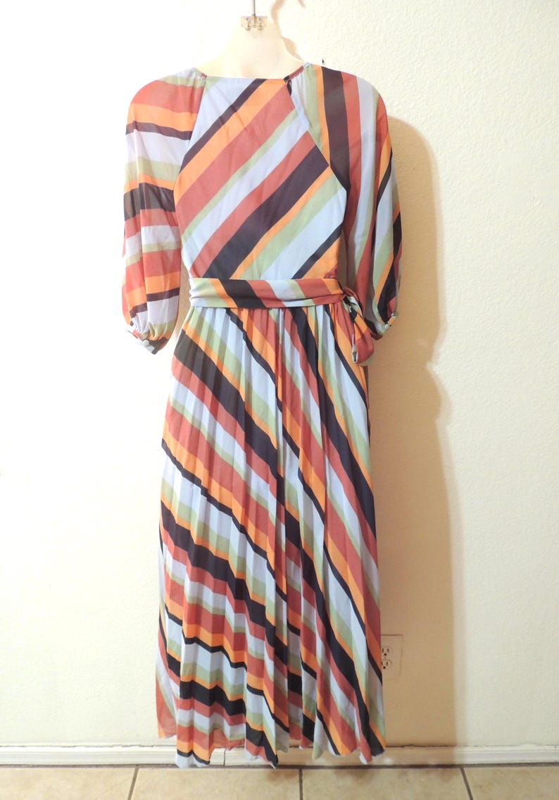 May include: A vintage, floor-length dress with a colorful striped pattern. The dress features a round neckline, long sleeves, and a matching belt. The stripes include orange, brown, black, and blue hues.