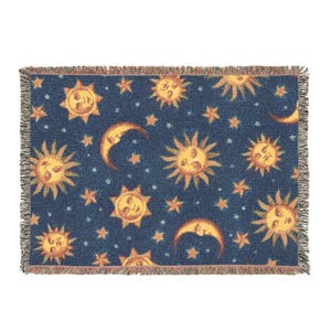 Op de afbeelding: Een rechthoekige sprei met een marineblauwe achtergrond. De sprei heeft een herhalend patroon van lachende zonnen, halve manen en sterren in tinten geel en oranje. De randen zijn gefranjerd.