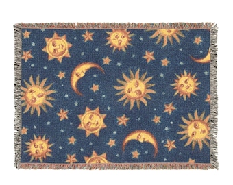 May include: A rectangular throw blanket with a navy blue background. The blanket features a repeating pattern of smiling suns, crescent moons, and stars in shades of yellow and orange. The edges are fringed.