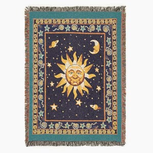 May include: A woven throw blanket featuring a celestial design. The center showcases a smiling sun surrounded by stars, planets, and a crescent moon against a dark blue background. The border is teal with decorative elements.