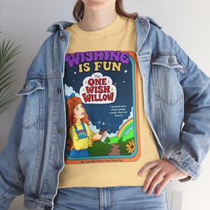 May include: A light yellow t-shirt with a graphic that reads "WISHING IS FUN" and "The ONE WISH WILLOW." The graphic features a cartoon illustration of a girl, a rainbow, and the text "Be Careful What You Wish For."