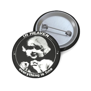 Op de afbeelding: Zwart-witte button met de tekst "IN HEAVEN" en "everything is fine" rond een vintage baby-afbeelding. De button heeft een zwarte rand en een zilveren pinback. Een tweede button is zichtbaar.