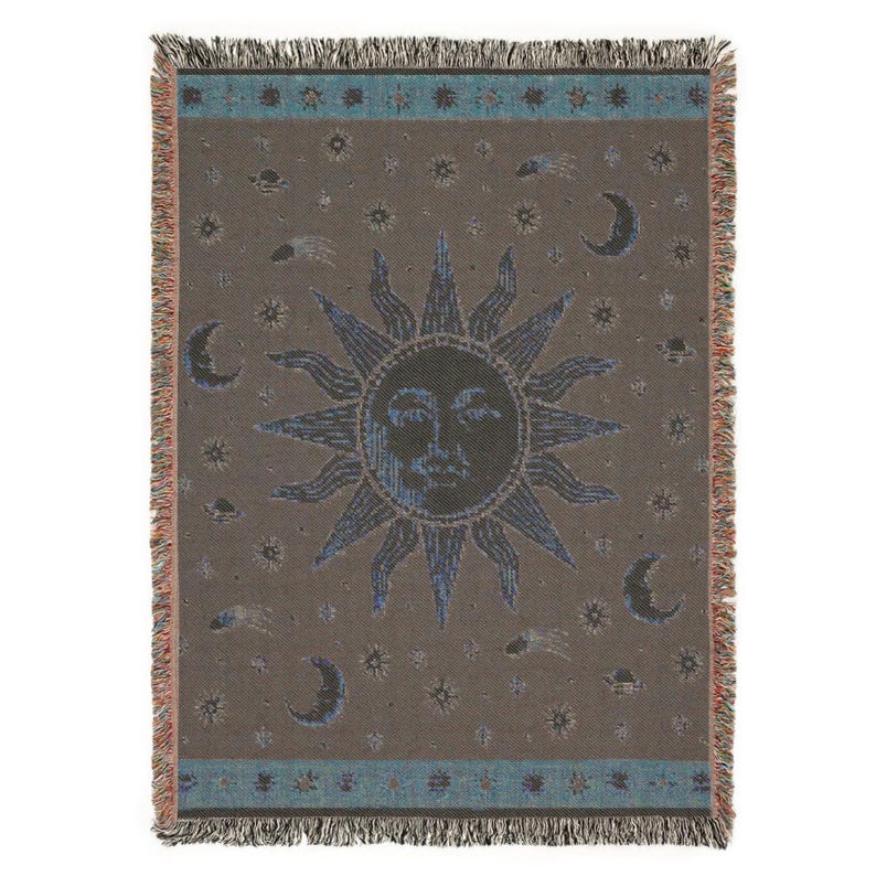 May include: A rectangular woven throw blanket featuring a central sun face with radiating rays, surrounded by crescent moons, stars, and comets. The design uses a brown background with blue and cream accents, finished with a fringed edge on all sides.