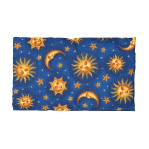 Puede incluir: Una tela rectangular con un diseño celestial. La tela presenta un fondo azul oscuro adornado con soles dorados, lunas crecientes y estrellas. Los soles y las lunas tienen caras sonrientes, creando un patrón caprichoso y artístico.