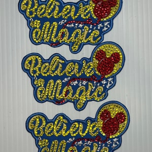 May include: Three blue and yellow embroidered patches with the words "Believe in Magic" and a red Mickey Mouse balloon.