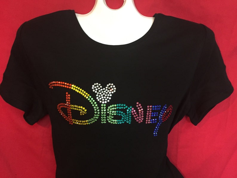 May include: Black short-sleeved t-shirt with the word "Disney" spelled out in colorful rhinestones. The "D" and the "y" are in a rainbow gradient, and the "i" is a Mickey Mouse head shape.