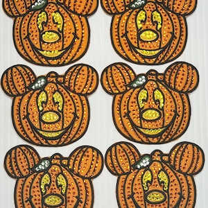 May include: Six orange and brown pumpkin-shaped patches with a Mickey Mouse face design. Each patch is covered in sparkly rhinestones and has a green stem.