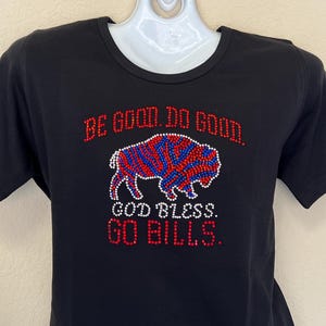 May include: Black t-shirt with a red, white, and blue rhinestone buffalo design. The shirt has the text "Be good. Do good. God bless. Go Bills." in rhinestones.