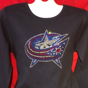 May include: A navy blue long-sleeved shirt with a rhinestone design of the Nashville Predators hockey team logo. The logo is in the team's colors of blue, red, and white.