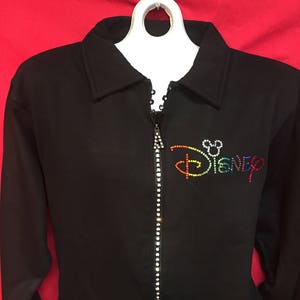 May include: Black zippered jacket with a rainbow rhinestone "Disney" logo on the front.