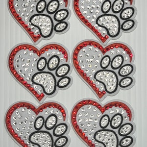 May include: Six red and white heart-shaped patches with a paw print design. Each patch is covered in rhinestones.