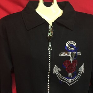 May include: Black zippered jacket with a rhinestone anchor design. The anchor is red, white, and blue.