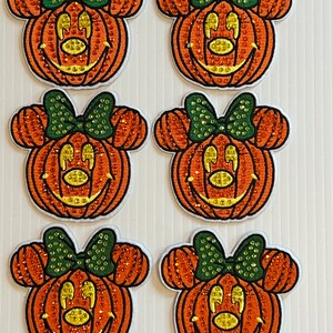 May include: Six orange and green Halloween pumpkin patches with a Minnie Mouse face and a green bow. The patches are covered in rhinestones.