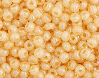 May include: A close-up image of a large quantity of small, round, light beige seed beads with a subtle iridescent shimmer.