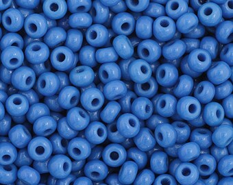 May include: A close-up view of a large quantity of small, round, opaque blue glass beads. The beads are all the same size and shape, and they are arranged in a random pattern.